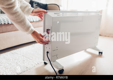 Using heater at home in winter. Woman regulating temperature on heater on wearing warm clothes. Heating season. Stock Photo