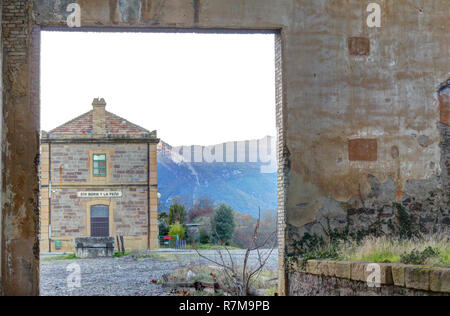 Abandoned train warehouse, with missing tiles from the roof, grass and ruined walls next to the railway in Santa Maria y La Peña train station, Spain Stock Photo