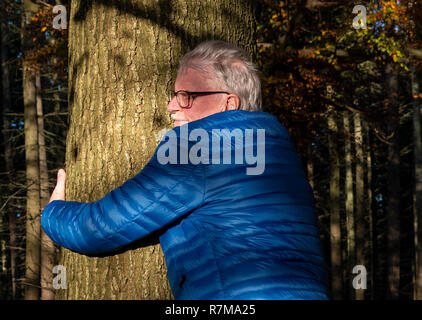 Mature man hugging a tree in a wood at Checkendon, South Oxfordshire, England, UK Stock Photo