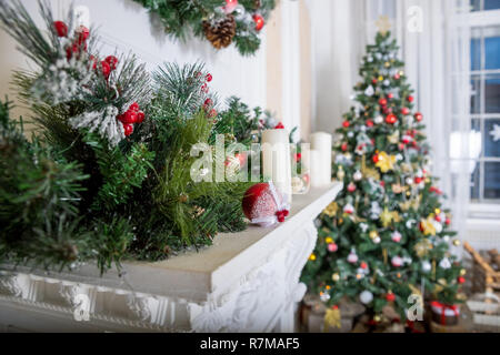 A cozy living room lighted with numerous lights decorated ready to celebrate Christmas. Christmas room interior design, Xmas tree decorated by lights, candles and garland lighting indoors fireplace. Stock Photo