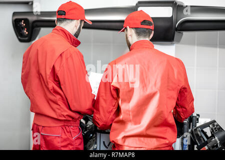 Auto mechanics in red uniform working with computer doing wheel allignment at the car service Stock Photo