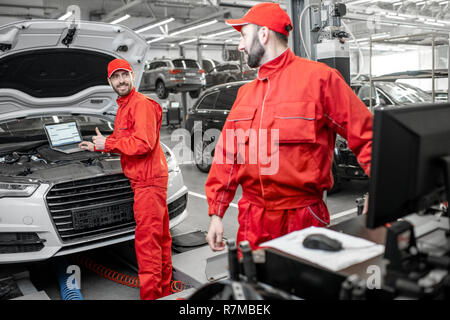 Two auto mechanics in red uniform doing engine diagnostics with computer in the car service Stock Photo