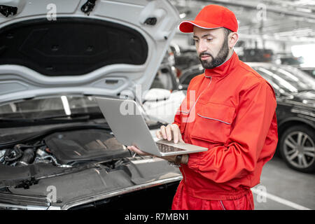Two auto mechanics in red uniform doing engine diagnostics with computer in the car service Stock Photo
