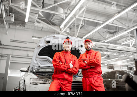 Portrait of a two handsome auto mechanics in red uniform standing together at the car service Stock Photo