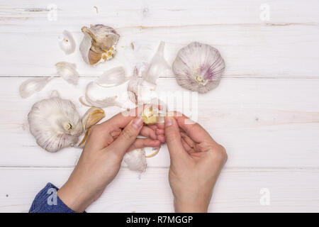 Woman hands are spliting garlic cloves. recipe step by step baked potatoes with onion flatlay on white wood Stock Photo