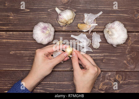 Woman hands are spliting garlic cloves. recipe step by step baked potatoes with onion flatlay on brown wood Stock Photo