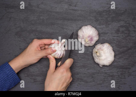Woman hands are spliting garlic cloves. recipe step by step baked potatoes with onion flatlay on grey stone Stock Photo