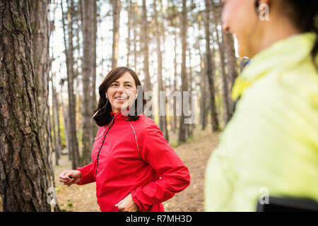 Female runners with earphones jogging outdoors in forest. Stock Photo