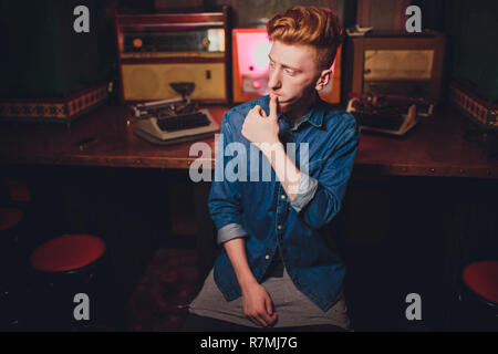 Young man writing on old typewriter. in dark lighting, restaurant, modern clothes, old writer habits Stock Photo
