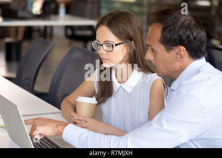Middle aged mentor helping intern with computer work Stock Photo