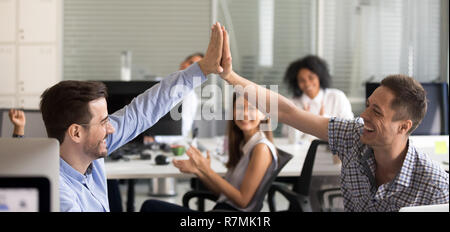 Happy young male colleagues giving high five, celebrate success Stock Photo