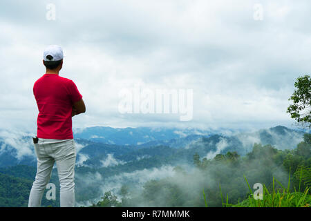 A man hiker standing on a cliff,Tropical mountain range view. View over Titiwangsa mountain range. Rainforest view at Royal Belum State Park. Stock Photo