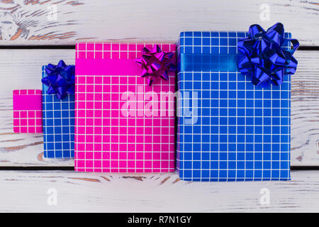 Group of gift boxes on wooden background. Present boxes packed in pink and blue paper on vintage wooden background. New Year or Christmas gifts. Stock Photo