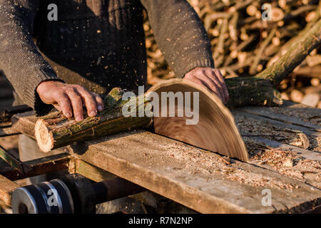 Man cutting wood using stationary circular saw outdoors in the sun. Stock Photo