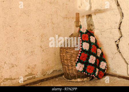 A large old of wine bottle in wicker basket covered with an ethnic bag.