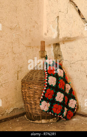 A large old of wine bottle in wicker basket covered with an ethnic bag.