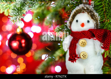Christmas snowman hanging on a fir tree branch on shiny background with copy space for text. Selective focus. Stock Photo