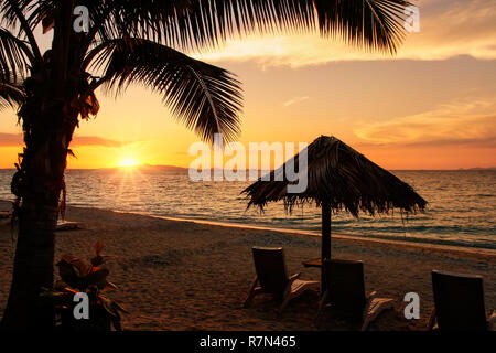 Silhouetted sun chairs with thatched umbrella on a beach at sunrise, South Sea Island, Mamanuca group, Fiji. Stock Photo