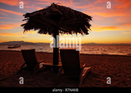 Silhouetted sun chairs with thatched umbrella on a beach at sunrise, South Sea Island, Mamanuca group, Fiji. Stock Photo