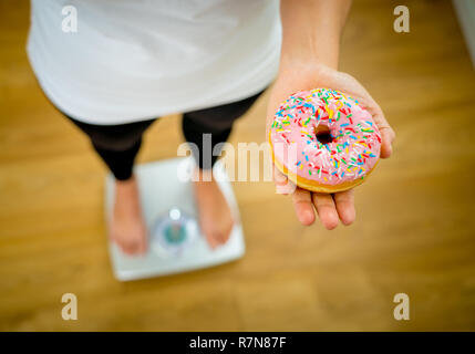 Close up of woman on scale holding on hands apple and doughnut making choice between healthy unhealthy food dessert while measuring body weight in Nut Stock Photo