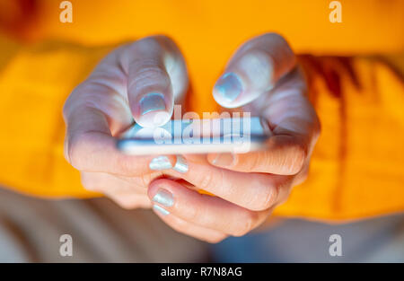 Close up of teenager or adult woman playing online and sending text on smart phone with a colorful background light from the screen in Mobile addictio Stock Photo