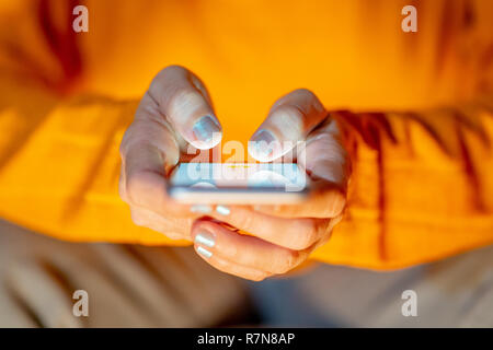 Close up of teenager or adult woman playing online and sending text on smart phone with a colorful background light from the screen in Mobile addictio Stock Photo