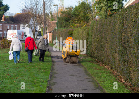 Roadside workers drilling into tarmac path, elderly woman having to walk around, ashford, uk Stock Photo
