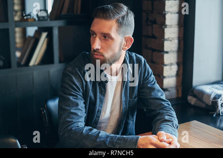 Young man sitting in a cafe at the table and waiting for the waiter with a menu to make an order. Restaurant customer. Business lunch Stock Photo