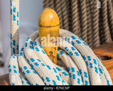 Close-up of bundled ropes on the deck of a sailboat. Detail of wooden cleats with nautical moored ropes. Stock Photo