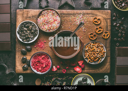 Homemade chocolate bars making. Various toppings and flavorings ingredients in bowls with melted chocolate on dark rustic kitchen table background, to Stock Photo