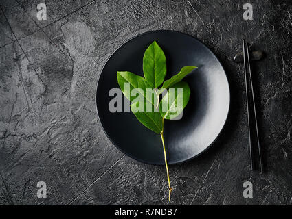 Dark empty plate of asian food with black chopsticks on black slate board. Asian style of food. Stock Photo