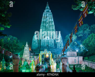 Long exposure of the illuminated Mahabodhi Temple in Bodh Gaya, with people moving in and out, and little flags waving in the wind, against a dark sky Stock Photo