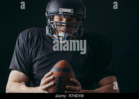 American football player in black sportwear with a ball on black background Stock Photo