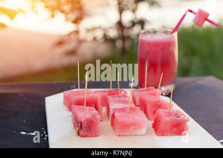 Glass of juice and cubic slices of watermelon on the cutting board. at outdoors in the garden. Summer time. Stock Photo