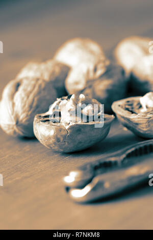 Walnut cracked open with nutcracker on wooden background with colour toning Stock Photo