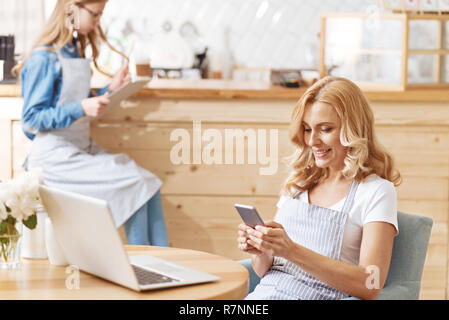 Mature woman wearing apron using smartphone in cafe Stock Photo
