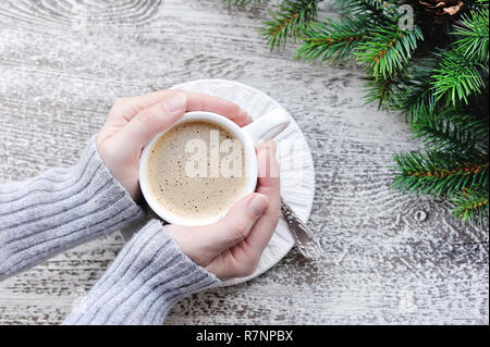 Female hands holding cups of coffee and fir branches on wooden table background Stock Photo