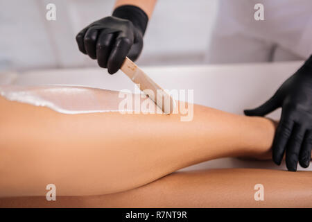 Master in hair removal holding legs of her client while putting wax on Stock Photo