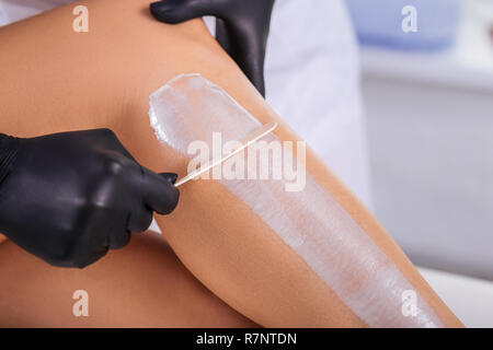 Master in hair removal wearing black gloves putting wax on Stock Photo