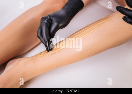 Master in hair removal making sugaring for her client lying on bed