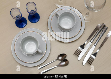 On the table, two cups with saucers, glasses, knives, spoons, forks on a napkin. The view from the top. Stock Photo