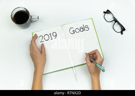 New Year, new me concept. Top view of female hands writing '2019 goals' in a copy book on white table Stock Photo
