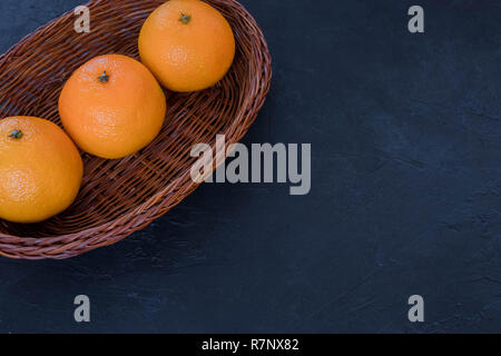 Tangerines in a basket, Christmas decor on a dark background. The concept of holidays. View from above. Dark rustic style. space under the text. Stock Photo