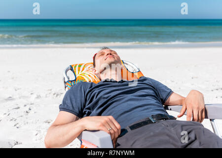 Young man millennial sleeping on beach chair during sunny day in Florida, lying reclining back, ocean horizon, white sand, gulf of mexico Stock Photo