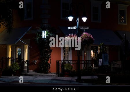 Naples, USA - April 29, 2018: Illuminated lights with hanging flower basket on lamp post pole on avenue street corner in Florida downtown beach city t Stock Photo