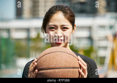 outdoor portrait of beautiful young asian girl holding a basketball looking at camera smiling. Stock Photo