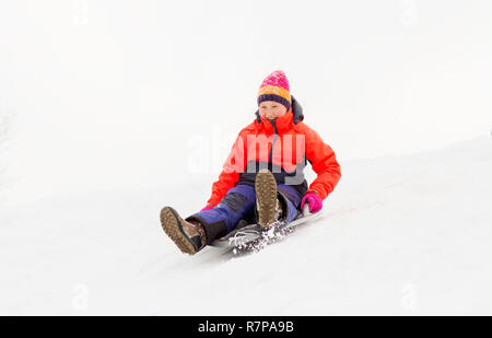 girl sliding down on snow saucer sled in winter Stock Photo