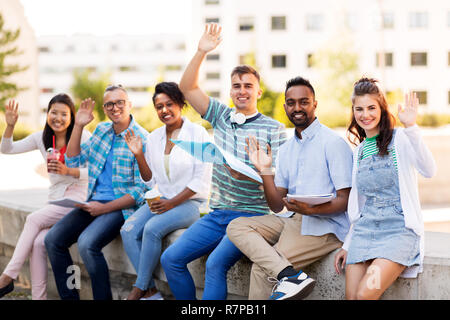 students with notebook waving hands outdoors Stock Photo