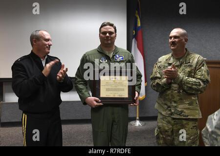 U.S. Army Maj. Gen. Greg Lusk (left), the Adjutant General of North Carolina, commander of the North Carolina National Guard, and U.S. Army Command Sgt. Maj. John Swart (right), the Command Sergeant Major of the North Carolina National Guard, give a round of applause to U.S. Air Force Maj. Nathan Barron (center), 156th Airlift Squadron, after presenting him with the North Carolina National Guard Soldier and Airman Medal for heroism during a ceremony held at the North Carolina Air National Guard Base, Charlotte Douglas International Airport, April 1, 2017. Barron acted decisively and courageous Stock Photo