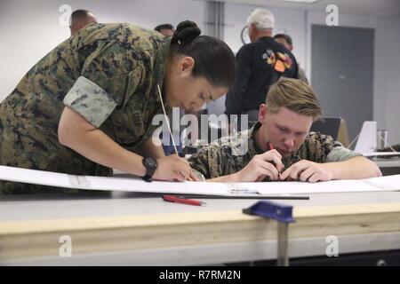 Petty Officer 2nd Class Leyla Coba, cryptologic technician technical, and Cpl. Dylan Lemaistre, signals intelligence and electronic warfare, Tactical Training Exercise Control Group, carve out the wing of a drone at the Fabrication Laboratory aboard Marine Corps Air Ground Combat Center, Twentynine Palms, Calif., March 29, 2017. The newly established FabLab is the first of its kind in the Marine Corps and will provide Marines and sailors the opportunity to develop avant-garde solutions to common problems through utilizing 3D printing technology. Stock Photo